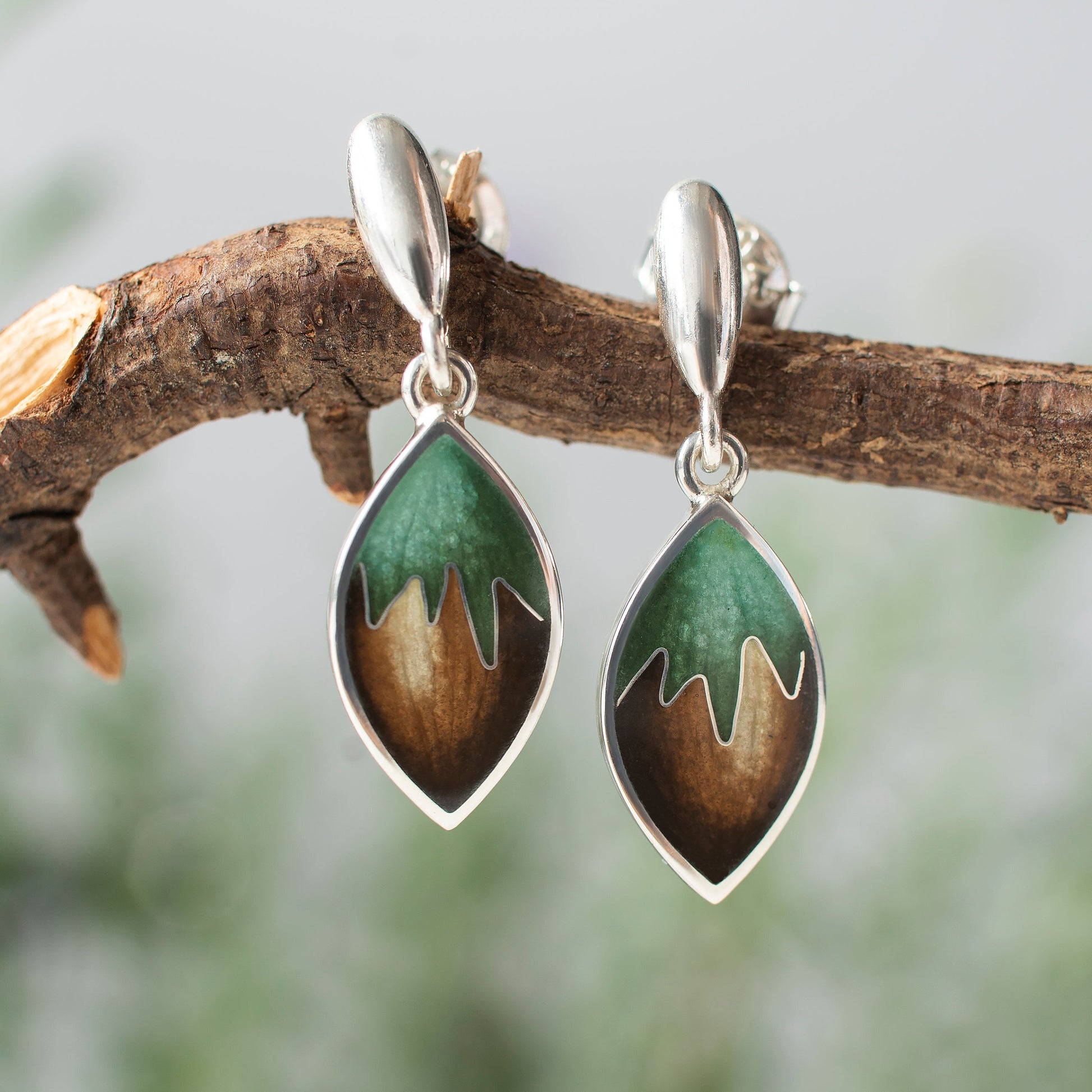 Teardrop-shaped earrings with nature-themed design hanging on a branch
